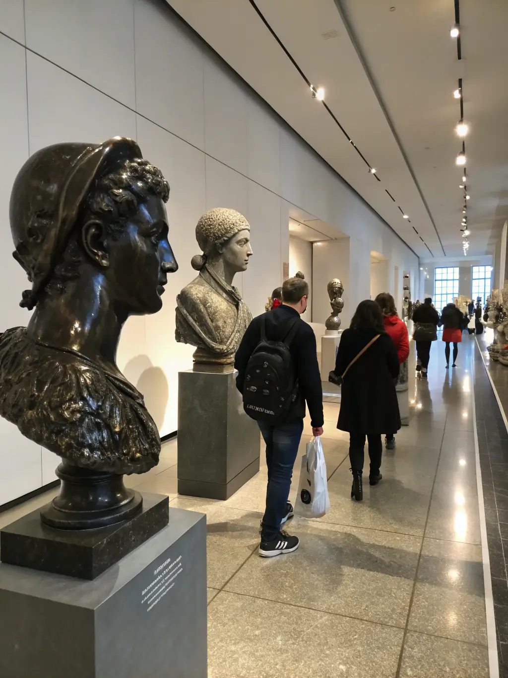 A photograph of a sculpture exhibition organized by LES ARTS DU ROY, showcasing a variety of three-dimensional artworks, with visitors admiring the pieces in a gallery setting.