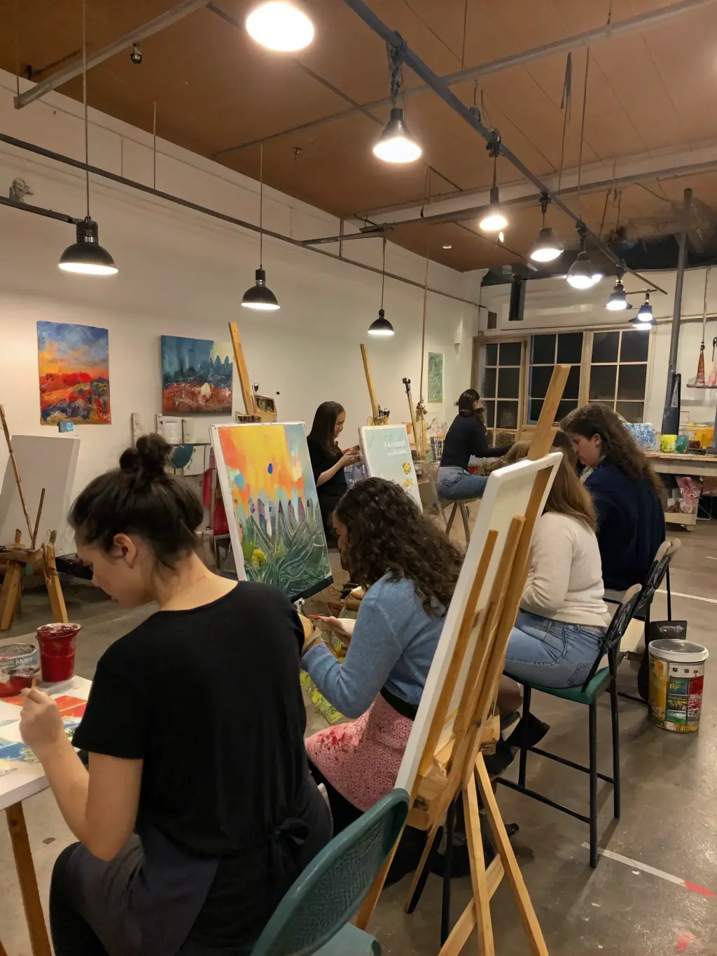 A vibrant photograph capturing participants actively engaged in a painting workshop at LES ARTS DU ROY, showcasing various age groups and skill levels, with easels, canvases, and art supplies visible in a well-lit studio setting.